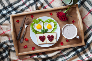 Breakfast in bed with heart-shaped eggs, toasts, jam, coffee, rose and petals. Valentines Day surprise.