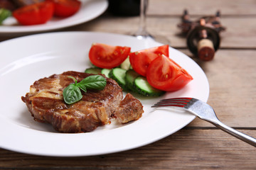Roasted beef fillet and fresh vegetables on plate, on wooden background