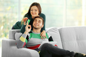 Young happy couple using credit card with tablet at home on light background