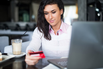 Woman doing online shopping at cafe, holding credit card typing numbers on laptop computer.