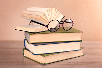 Pile of books and eyeglasses on it on wooden table, close up