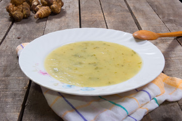 soup of Jerusalem artichoke in white plate on plaid dishcloth with raw artichoke 