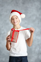 Boy in Santa hat with gift box on grey background