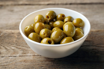 Fresh green olives in white bowl on wooden background