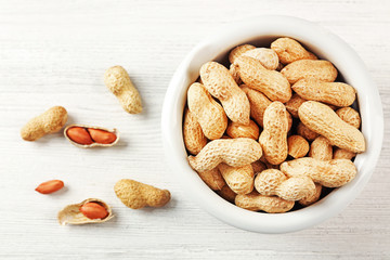 Peanuts in the bowl on white wooden background