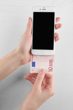 Hands holding smart phone and euro banknote on light table. Telephone charges