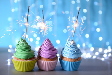 Varicolored cupcakes icing with sparklers in a row on a glitter background