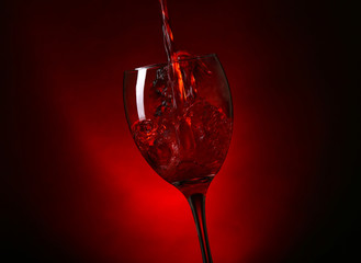 Wine pouring in glass on dark red background