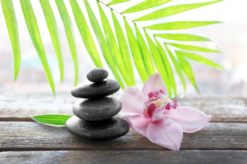 Spa stones with palm leaves and pink orchid on wooden background