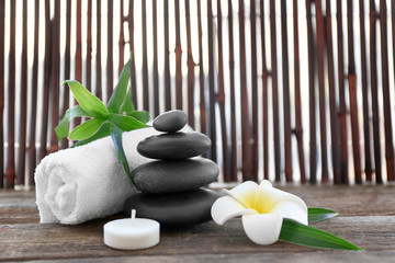 Spa stones with towel, bamboo, candle and tropical flower on wooden background