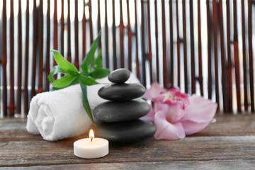 Spa stones with towel, candle, bamboo and pink orchid on wooden background