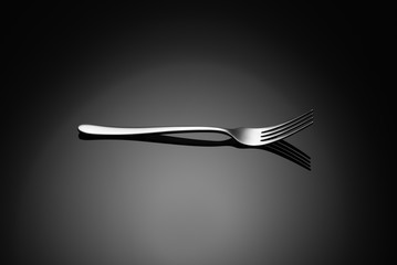 Stainless steel, modern silverware on black background with reflection.
