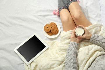 Woman with tablet drinking milk on her bed