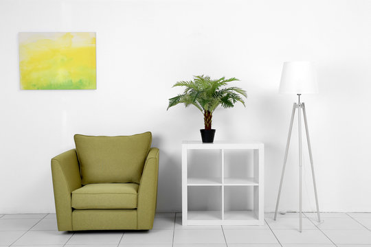 Living room interior with green armchair, white shelf and lamp on white wall background