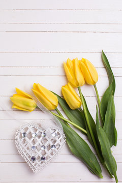 Yellow tulips flowers  and decorative heart on white painted wooden background. Selective focus. Place for text.