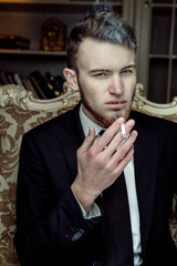 Close up portrait with casual young man sitting in vintage chair with a cigarette