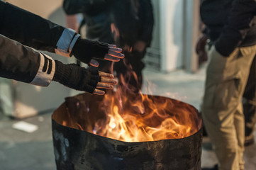 Homeless man warming his hands by a fire / Poor men warm outdoors near smoking barrel