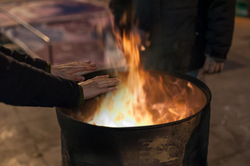 Homeless man warming his hands by a fire / Poor men warm outdoors near smoking barrel