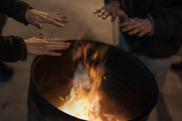 Homeless man warming his hands by a fire / Poor men warm outdoors near smoking barrel