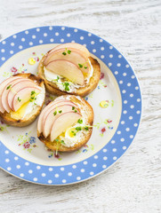 Open sandwich with goat's cheese, apple and honey on a light wooden board. Tasty breakfast, snack or appetizer with wine