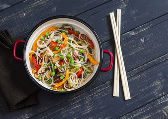 Stir fry vegetable with rice noodles in an enamel pot on dark wooden background