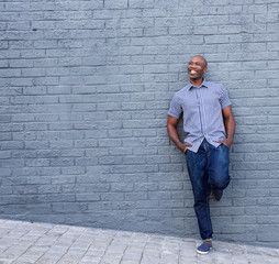 Fototapeta na wymiar Smiling african guy leaning against gray wall