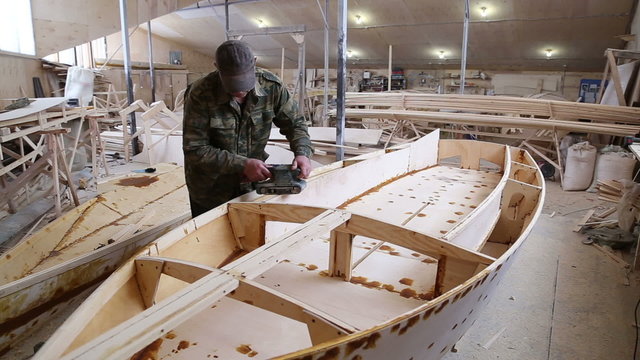 A carpenter polishes details wooden boat belt sander machine in the construction of boats at the shipyard
