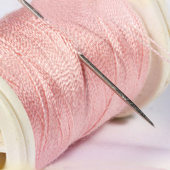 Detail view of needle in a pink spool of thread