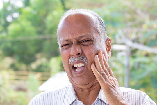 Closeup portrait elderly business man with tooth ache crown problem cavity grimacing from pain touching outside mouth with hand isolated outside background. Negative human emotion facial expression