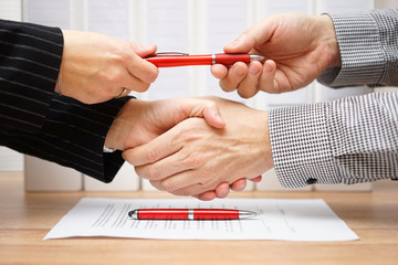 Business partners shaking hands and exchanging pen after finishe