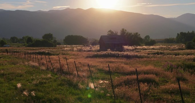 An old cabin sits behind a fence in a beautiful mountain meadow. 