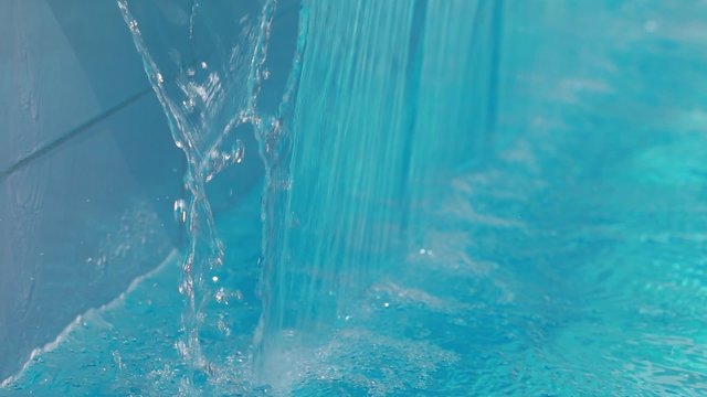 Refreshing of water in swimming pool. Waterfall at poolside, closeup

