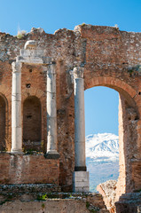 View of some columns in the stage of the greek theater in Taormina and a perspective of snowy mount Etna