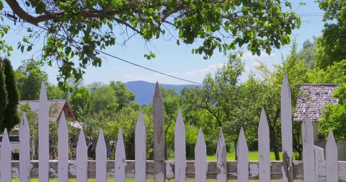 A white picket fence lines a yard on a quiet small town street.