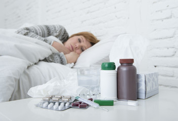 Obraz na płótnie Canvas sick woman feeling bad ill lying on bed suffering headache winter cold and flu virus having medicines