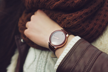 Elegant outfit. Closeup of brown wrist watch on the hand of stylish woman. Fashionable girl on the street. Female fashion. Toned