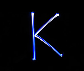 K Kilo alphabet hand writing blue light  over black background.