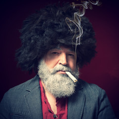 A bearded man in a hat and a cigarette in his mouth