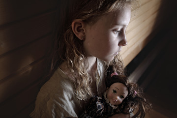 sad little girl with curly hair sitting confused with a doll