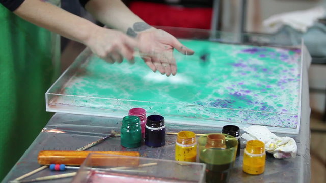 Purple oil-based inks splashing over green in a tank with water being prepared for marbling. The Ebru is a method of aqueous surface design
