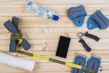Sport Equipment. Dumbbells,  Ankle Weights, Wrist Weights, Hand Grip, Towel, Tape Measure, Bottle Of Water, Smart Phone With Earphones On Boards. Sport Fitness Background