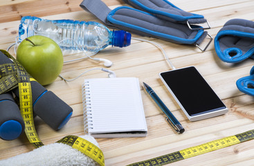 Sport Equipment. Dumbbells, Ankle Weights, Wrist Weights, Towel, Tape Measure, Bottle Of Water, Smart Phone With Earphones And Notebook To Workout Plan On Wooden Table. Sport Fitness Background