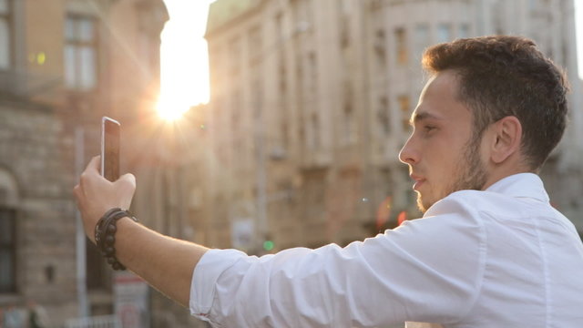   Attractive male in his 20s taking panorama picture by using his smartphone outdoors