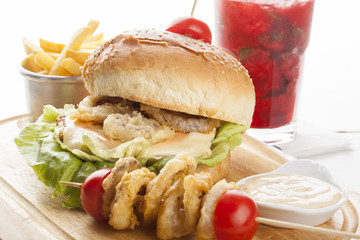 Delicious hamburger and french fries and onion rings on wooden b