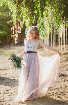 beautiful fabulous blonde curly boho bride with stylish rustical bouquet standing under tree on the beach