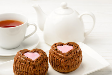 Chocolate muffins in shape of heart and cup of tea on wooden table.
