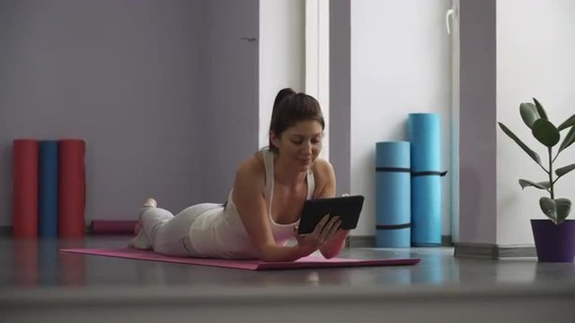 Girl lying on the yoga mat and looking at the tablet