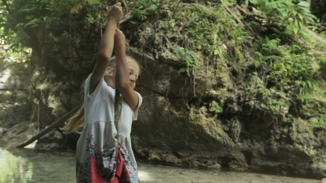 children girls playing hanging and climbing from lianas at the jungle forest park outdoor.young girl playing with a vine in the rain forest near the river.Travel concept.Family,summer vacation.