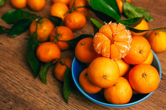 many fresh mandarin oranges in  blue bowl, standing on a wooden table