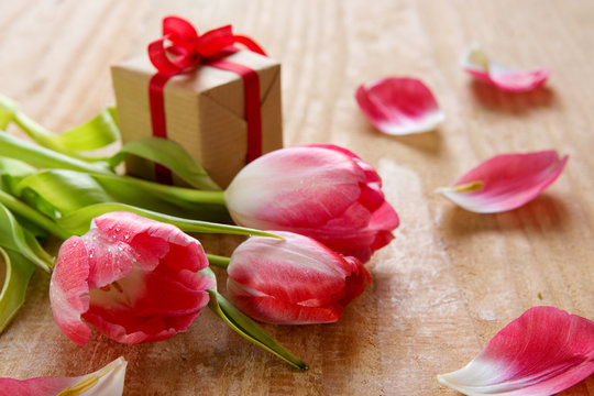 Pink tulips with gift on wood background.